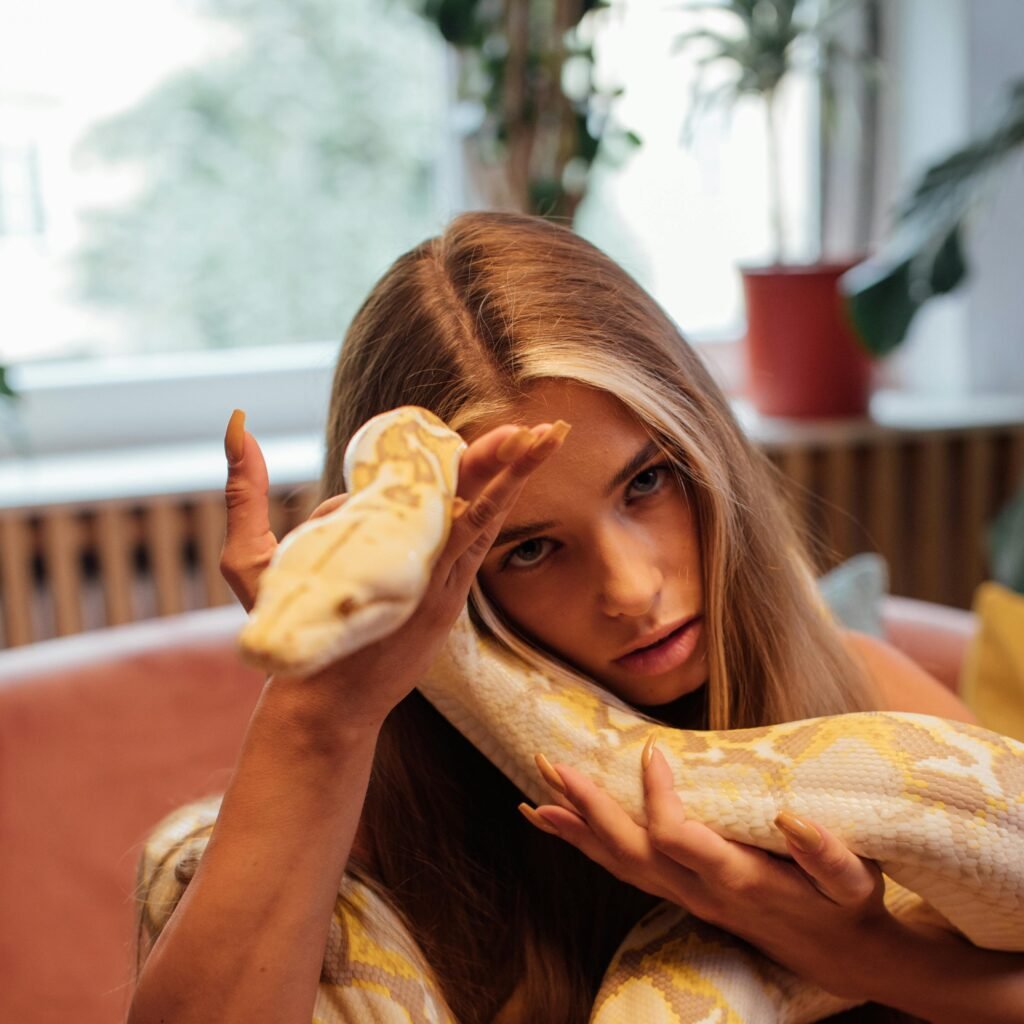Caucasian woman with a non-venomous snake on her shoulder indoors.